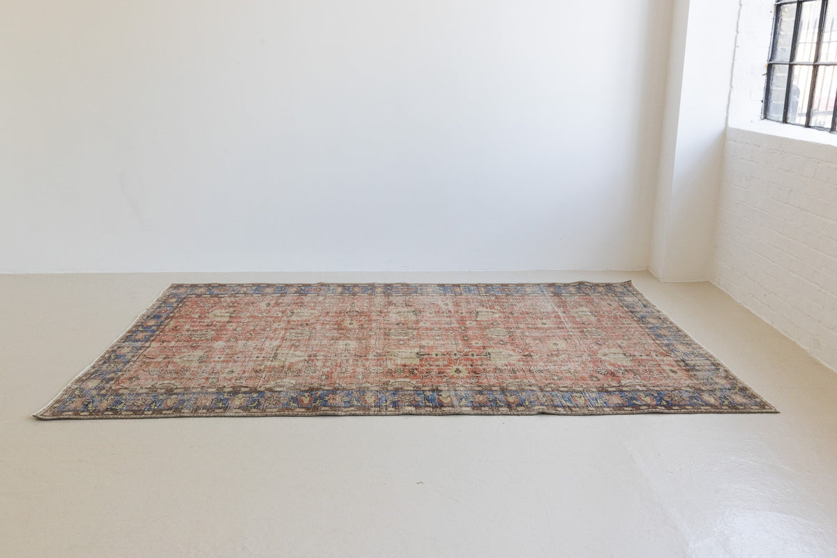 This is an large antique Turkish handwoven carpet in a rusty orange red  and muted blue with ivory tones. This vintage hand woven wool rug features a all over floral design.