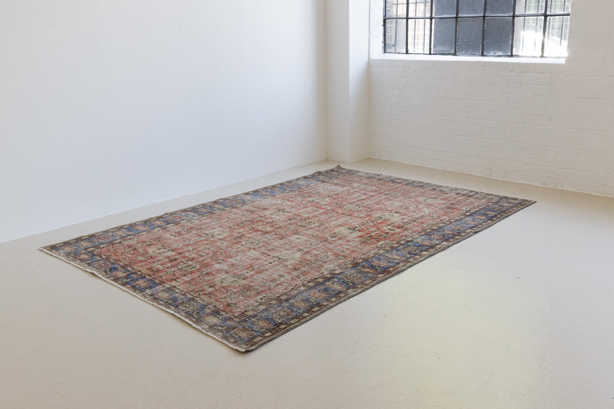 This is an large antique Turkish handwoven carpet in a rusty orange red  and muted blue with ivory tones. This vintage hand woven wool rug features a all over floral design.