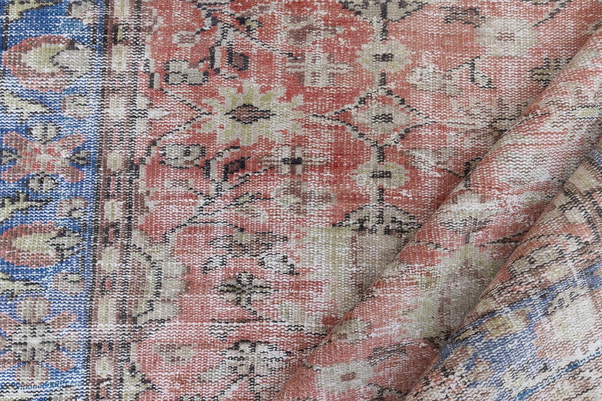 This is an large antique Turkish handwoven carpet in a rusty orange red  and muted blue with ivory tones. This vintage hand woven wool rug features a all over floral design.