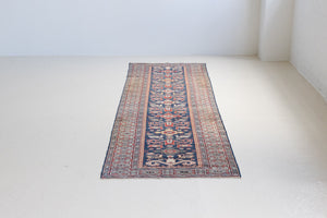 Beau is an antique Persian Caucasian runner in red and cream on a deep indigo ground, framed by a wide geometric border. Handwoven Caucasian carpets are prized for their bold geometric patterns and rich, saturated and jewel tones. 