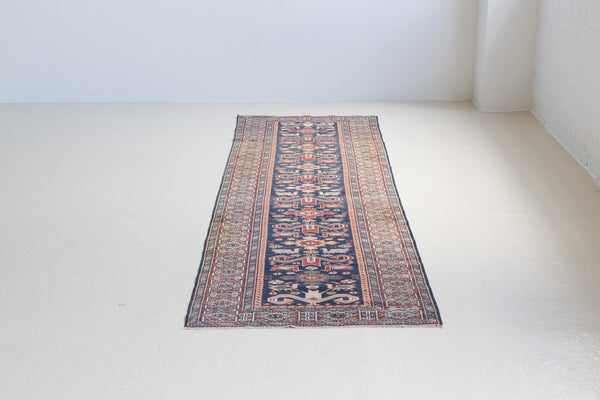 Beau is an antique Persian Caucasian runner in red and cream on a deep indigo ground, framed by a wide geometric border. Handwoven Caucasian carpets are prized for their bold geometric patterns and rich, saturated and jewel tones. 