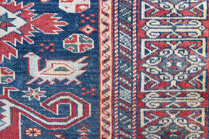 Beau is an antique Persian Caucasian runner in red and cream on a deep indigo ground, framed by a wide geometric border. Handwoven Caucasian carpets are prized for their bold geometric patterns and rich, saturated and jewel tones. 