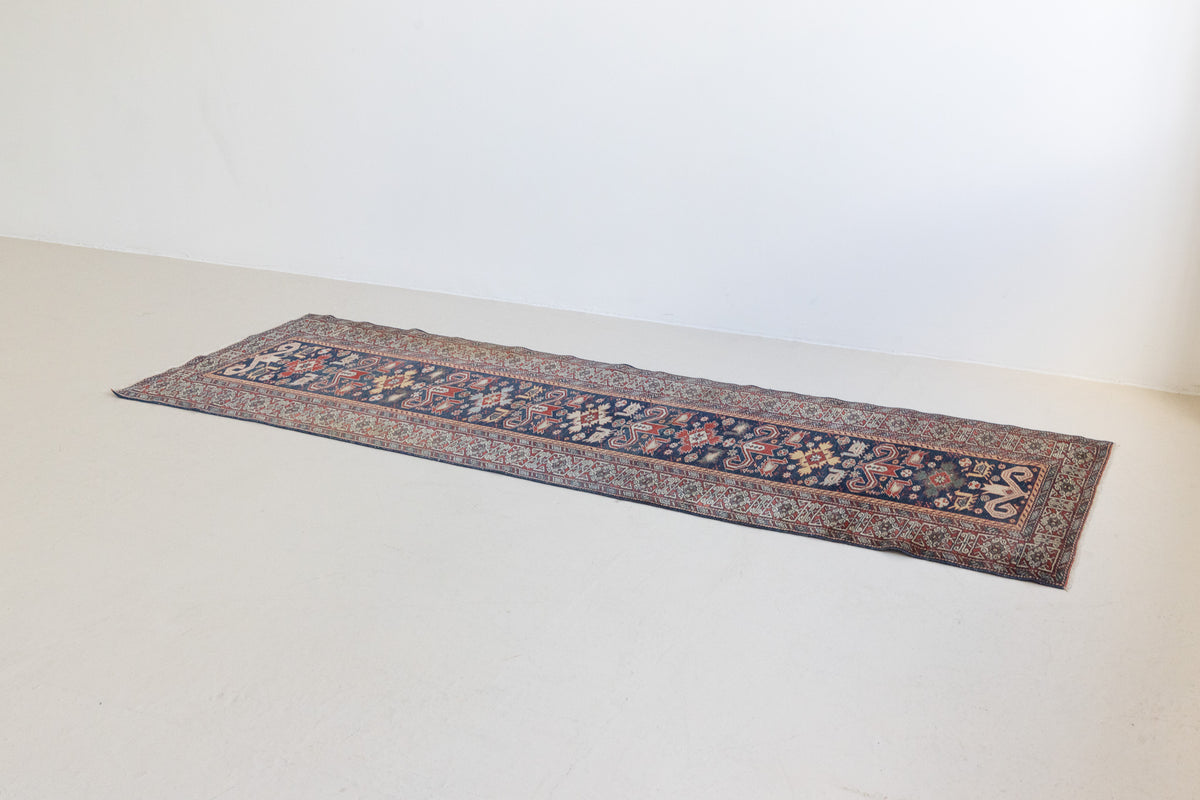 Beau is an antique Persian Caucasian runner in red and cream on a deep indigo ground, framed by a wide geometric border. Handwoven Caucasian carpets are prized for their bold geometric patterns and rich, saturated and jewel tones. 