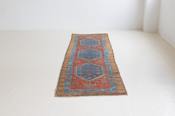 An antique Persian Heriz runner with three medallions in indigo blue set on a rust red field. Heriz rugs is one of the most recognisable Persian carpet designs, known for bold geometric pattern and vibrant colour.