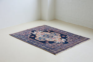 A small antique handwoven Persian Senneh rug, with an intricate ivory medallion in pink and blue set on a deep indigo field. Persian Senneh carpets are known for their fine, intricate patterns and distinctive weaving technique.