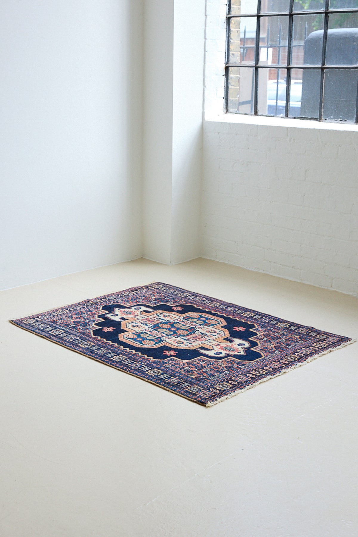 An antique handwoven Persian Senneh rug, with an intricate ivory medallion in pink and blue set on a deep indigo field. Persian Senneh carpets are known for their fine, intricate patterns and distinctive weaving technique.