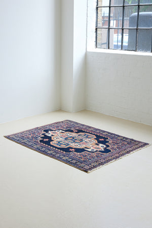 An antique handwoven Persian Senneh rug, with an intricate ivory medallion in pink and blue set on a deep indigo field. Persian Senneh carpets are known for their fine, intricate patterns and distinctive weaving technique.