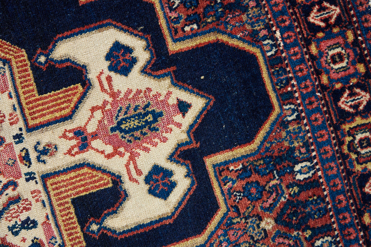 An antique handwoven Persian Senneh rug, with an intricate ivory medallion in pink and blue set on a deep indigo field. Persian Senneh carpets are known for their fine, intricate patterns and distinctive weaving technique.
