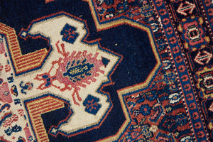 An antique handwoven Persian Senneh rug, with an intricate ivory medallion in pink and blue set on a deep indigo field. Persian Senneh carpets are known for their fine, intricate patterns and distinctive weaving technique.