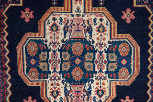 Close up of an antique handwoven Persian Senneh rug, with an intricate ivory medallion in pink and blue set on a deep indigo field. Persian Senneh carpets are known for their fine, intricate patterns and distinctive weaving technique.