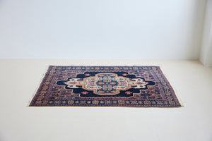 An antique handwoven Persian Senneh rug, with an ivory medallion in pink and blue set on a deep indigo field. Persian Senneh carpets are known for their fine, intricate patterns and distinctive weaving technique.