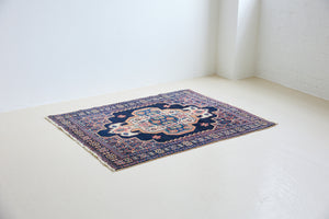 An antique handwoven Persian Senneh rug, with an intricate ivory medallion in pink and blue set on a deep indigo field. Persian Senneh carpets are known for their fine, intricate patterns and distinctive weaving technique.