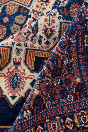 Close up of antique handwoven Persian Senneh rug, with an intricate ivory medallion in pink and blue set on a deep indigo field. Persian Senneh carpets are known for their fine, intricate patterns and distinctive weaving technique.