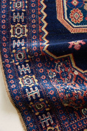 An antique handwoven Persian Senneh rug, with an ivory medallion in pink and blue set on an indigo field. Persian Senneh carpets are known for their fine, intricate patterns and distinctive weaving technique.