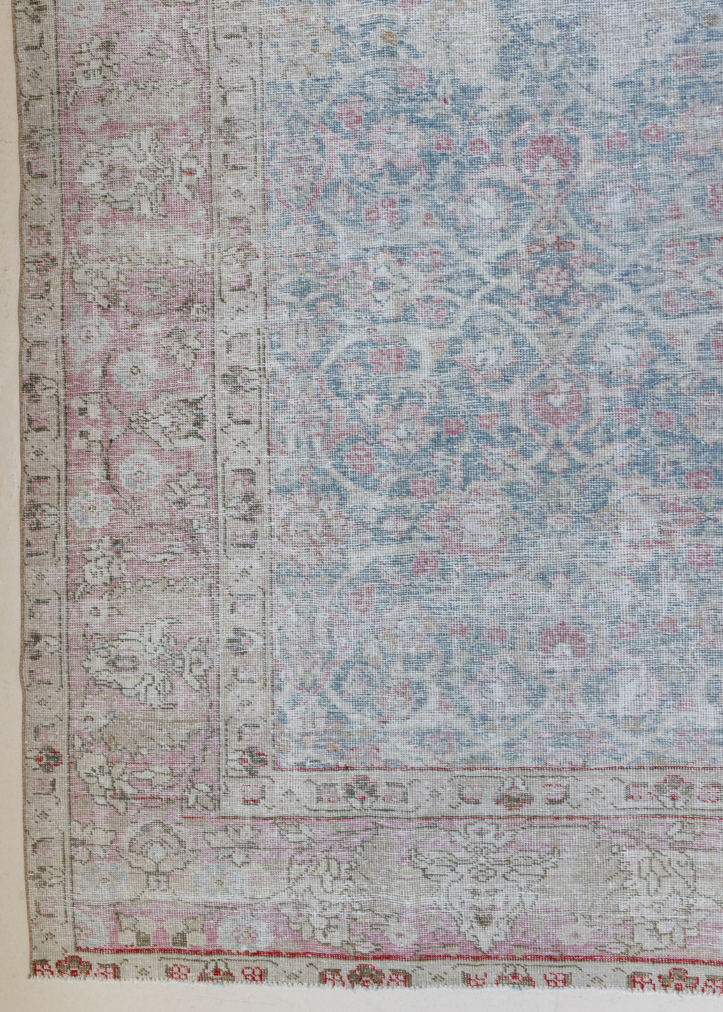 An antique Persian Tabriz rug. This large handwoven antique carpet features a lovely muted blue colour palette and a pink border alongside an intricate all over design.