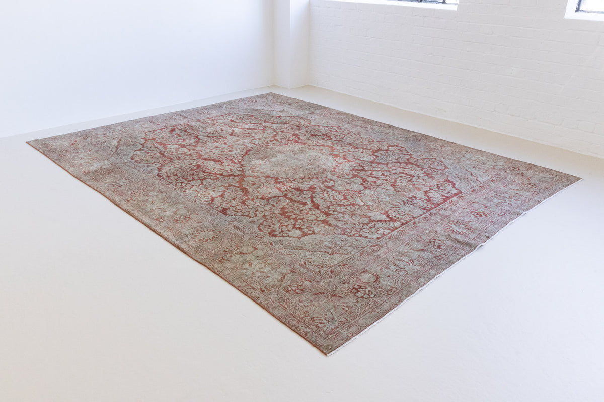 This is an antique Persian Sarouk rug, a handmade carpet in red and blue tones, featuring a floral medallion design.
