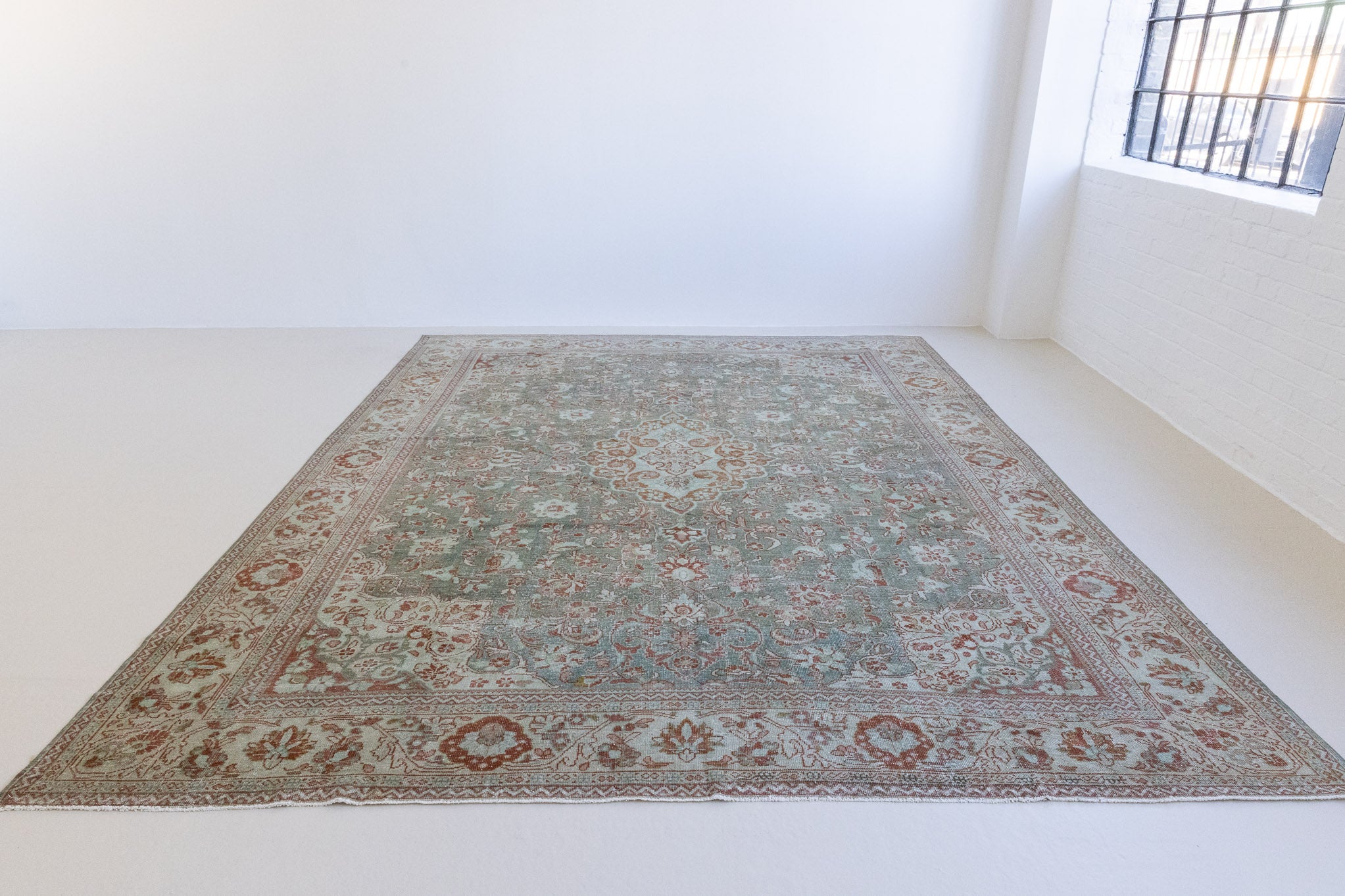 Electra is an antique Persian Tabriz rug with a lovely muted blue colour palette featuring a beautiful rustic red and ivory border alongside an intricate central medallion design within the vintage carpet. 