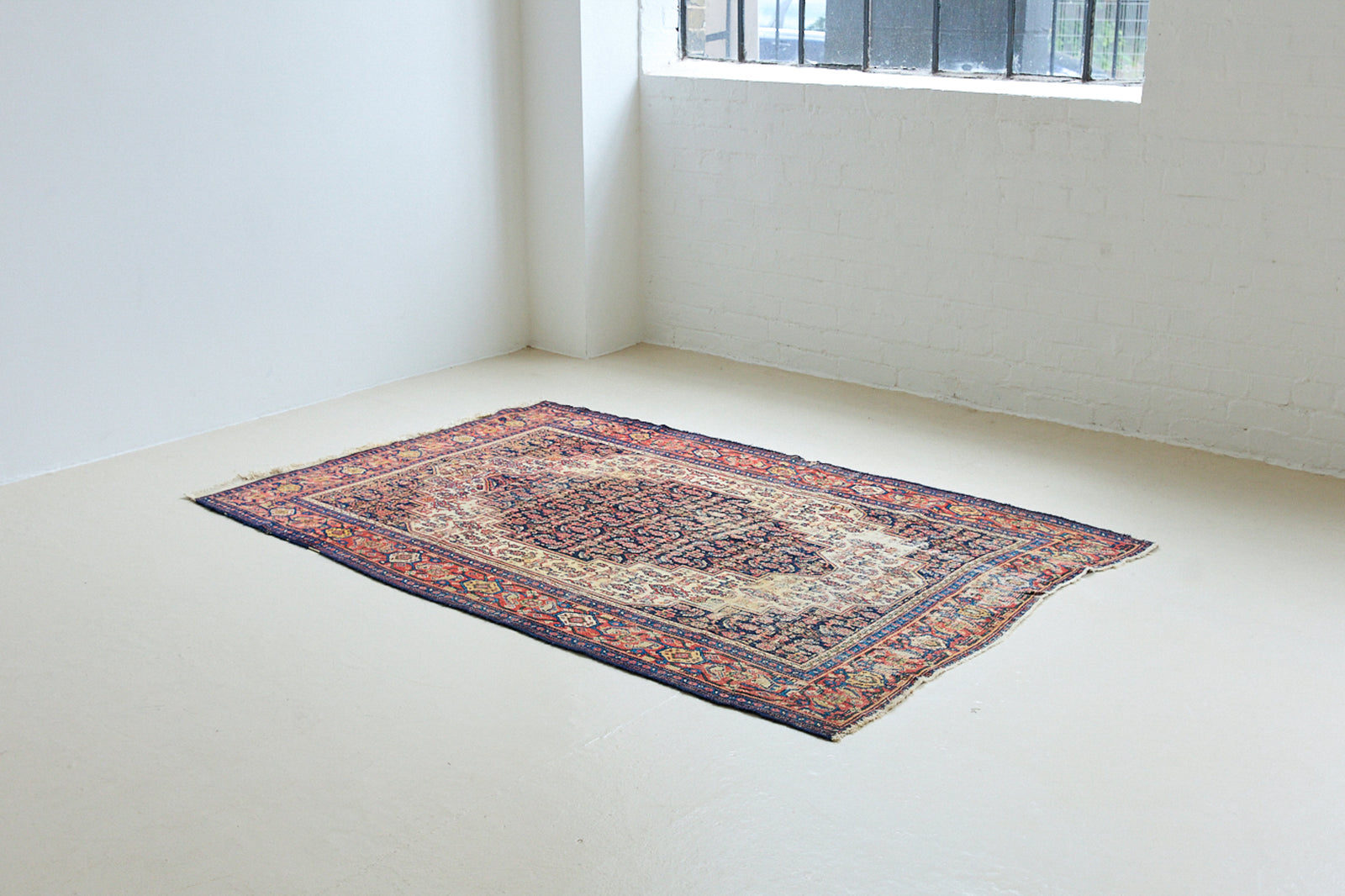 Raine is a beautiful antique Senneh rug with an intricate design. Senneh rugs are known for their fine and intricate patterns and distinctive weaving technique. Raine has a central motif surrounded by an intricate pattern and a pleasing colour palette of blue, red and taupe.