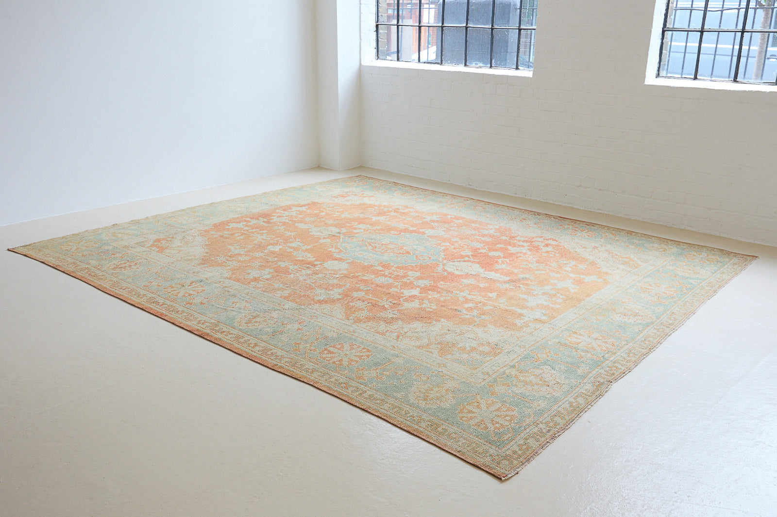 An antique Turkish Oushak rug. Perdita features a large-scale, open medallion pattern, flowing botanical motifs and a generous field space set against a blue and terracotta ground.