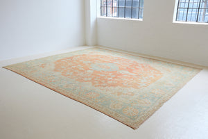 An antique Turkish Oushak rug. Perdita features a large-scale, open medallion pattern, flowing botanical motifs and a generous field space set against a blue and terracotta ground.