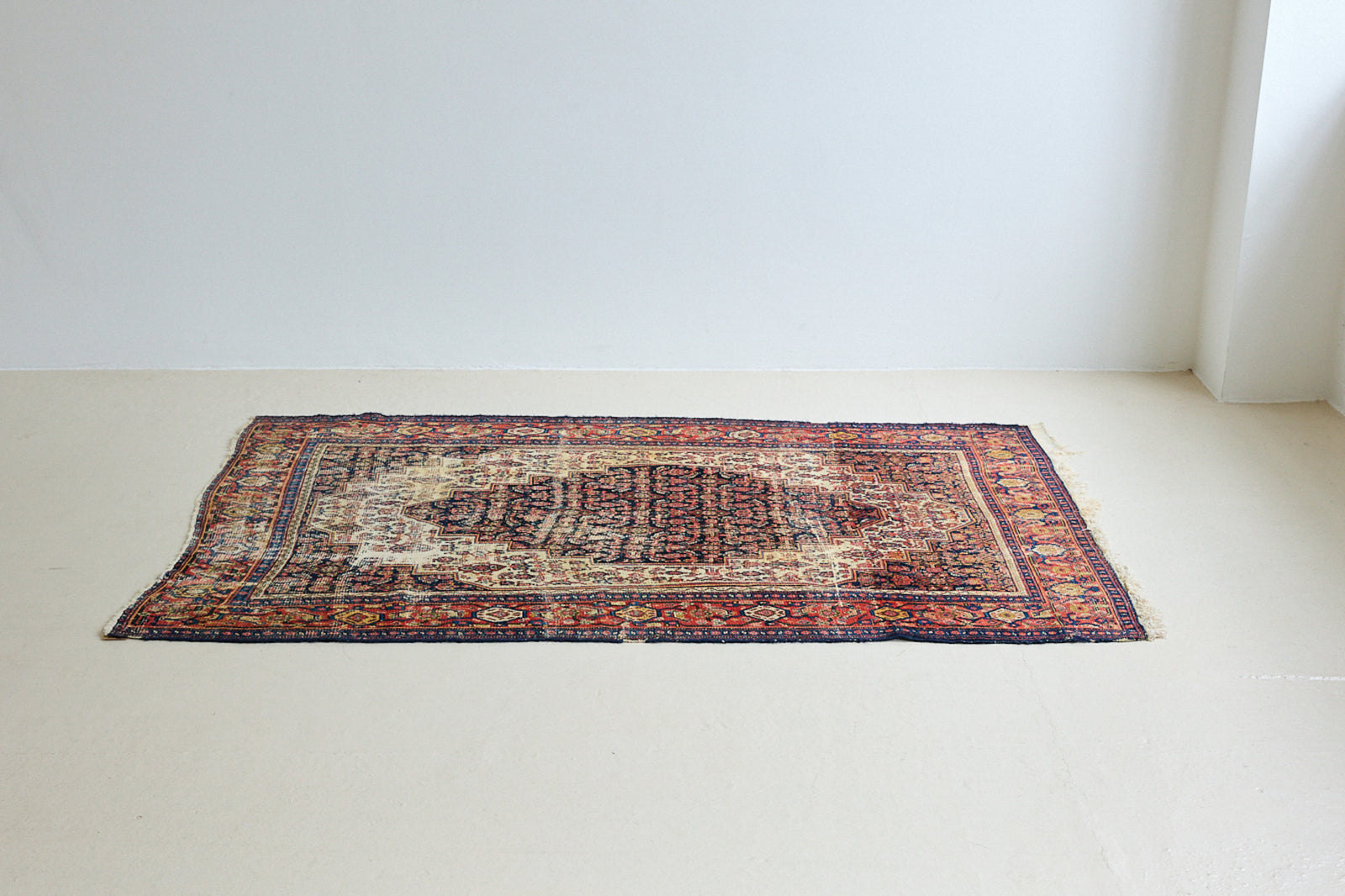 Raine is a beautiful antique Senneh rug with an intricate design. Senneh rugs are known for their fine and intricate patterns and distinctive weaving technique. Raine has a central motif surrounded by an intricate pattern and a pleasing colour palette of blue, red and taupe.