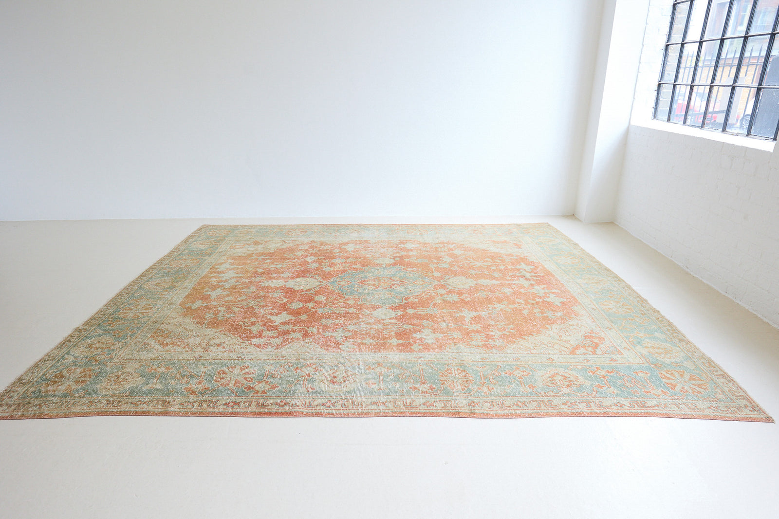 An antique Turkish Oushak rug. Perdita features a large-scale, open medallion pattern, flowing botanical motifs and a generous field space set against a blue and terracotta ground.