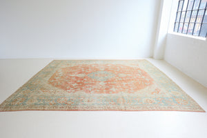 An antique Turkish Oushak rug. Perdita features a large-scale, open medallion pattern, flowing botanical motifs and a generous field space set against a blue and terracotta ground.