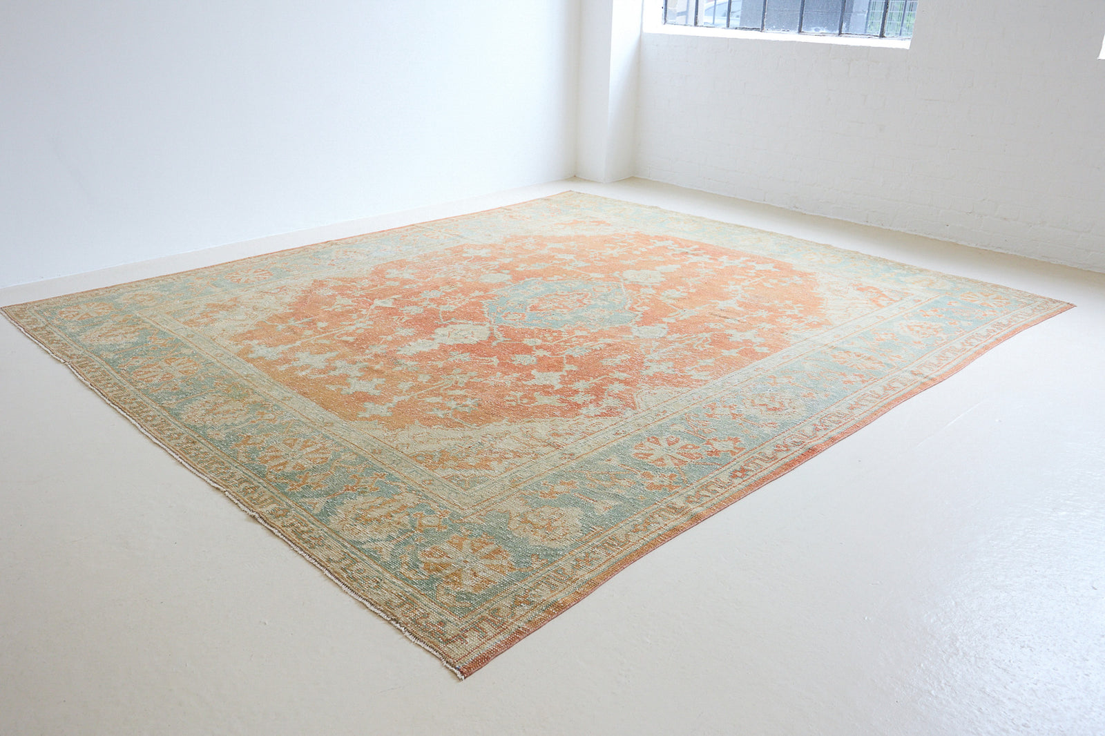 An antique Turkish Oushak rug. Perdita features a large-scale, open medallion pattern, flowing botanical motifs and a generous field space set against a blue and terracotta ground.