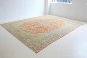 An antique Turkish Oushak rug. Perdita features a large-scale, open medallion pattern, flowing botanical motifs and a generous field space set against a blue and terracotta ground.