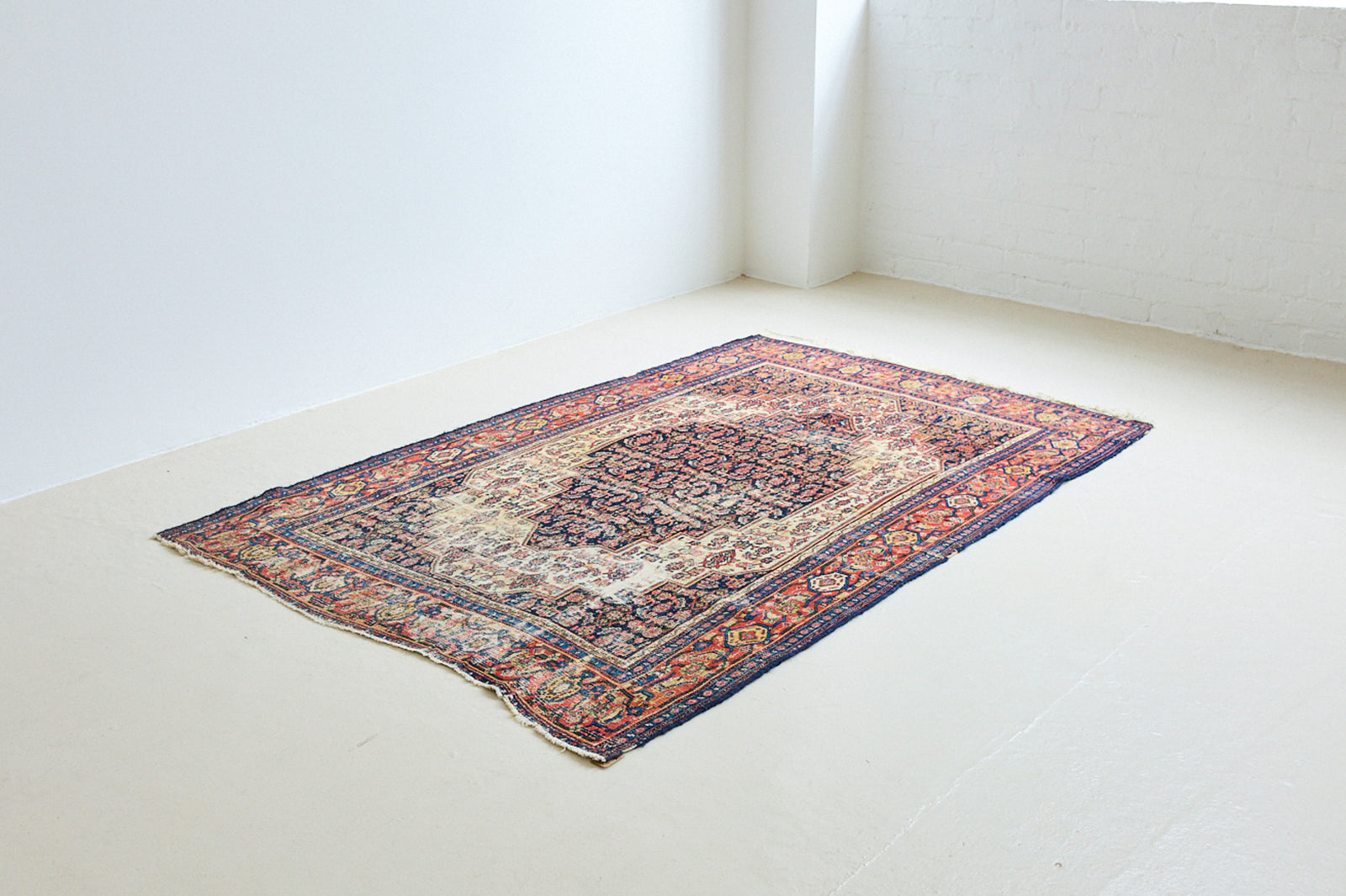 Raine is a beautiful antique Senneh rug with an intricate design. Senneh rugs are known for their fine and intricate patterns and distinctive weaving technique. Raine has a central motif surrounded by an intricate pattern and a pleasing colour palette of blue, red and taupe.