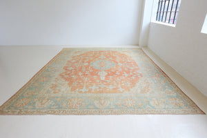 An antique Turkish Oushak rug. Perdita features a large-scale, open medallion pattern, flowing botanical motifs and a generous field space set against a blue and terracotta ground.