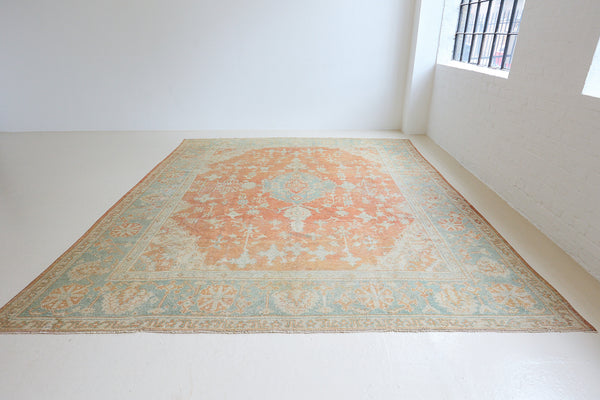 An antique Turkish Oushak rug. Perdita features a large-scale, open medallion pattern, flowing botanical motifs and a generous field space set against a blue and terracotta ground.