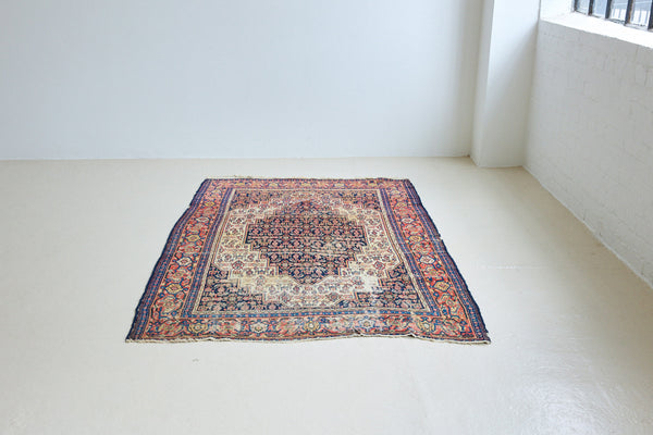 Raine is a beautiful antique Senneh rug with an intricate design. Senneh rugs are known for their fine and intricate patterns and distinctive weaving technique. Raine has a central motif surrounded by an intricate pattern and a pleasing colour palette of blue, red and taupe.