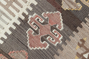 Close-up of an antique Anatolian kilim rug with geometric designs in brown, beige, and blue, featuring the traditional hand on hips motif
