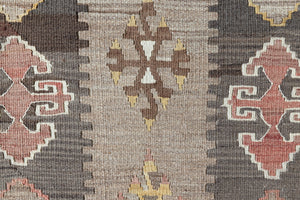 Close-up of an antique Anatolian kilim rug with geometric designs in brown, beige, and blue, featuring the traditional hand on hips motif