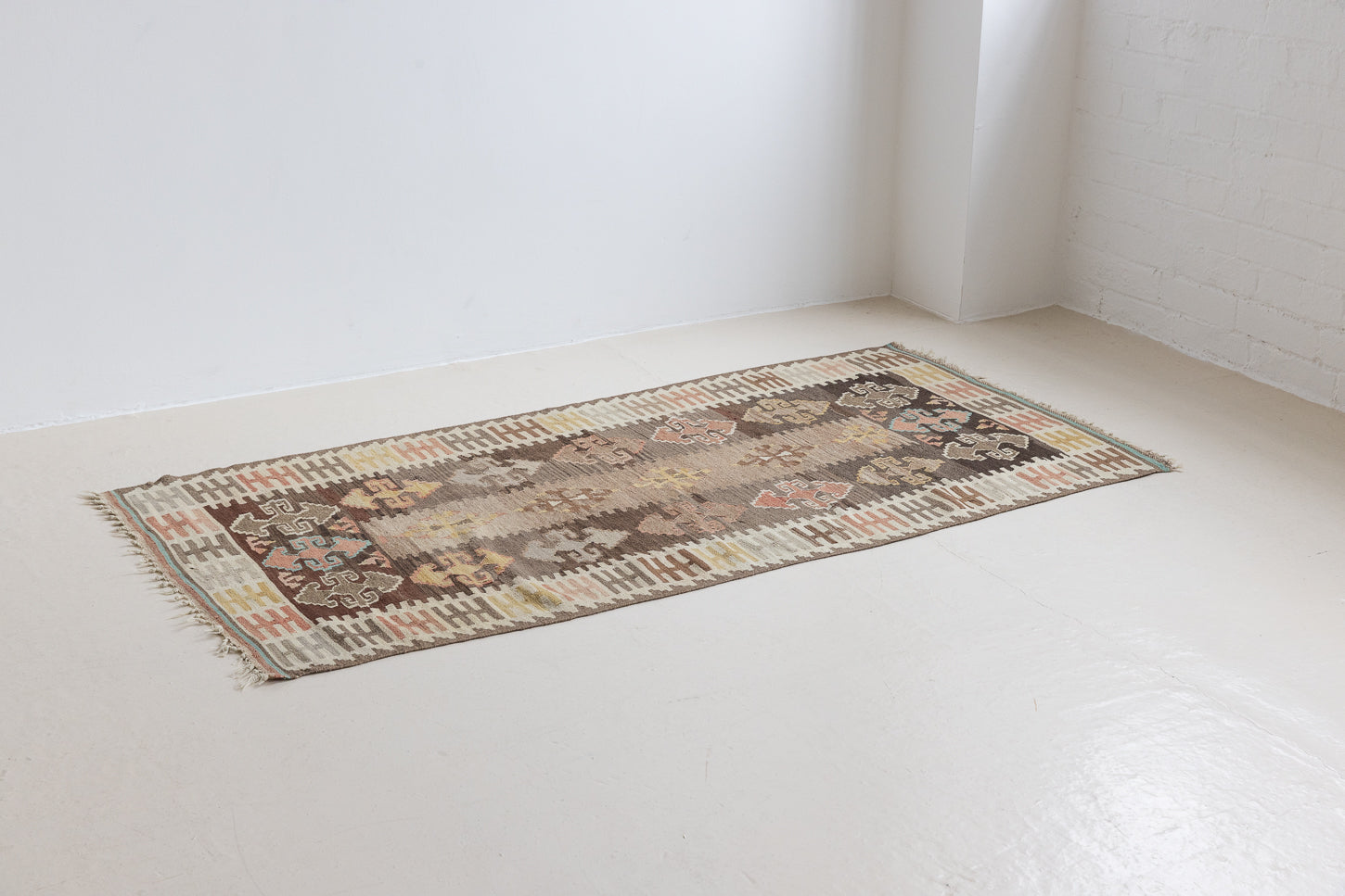 Close-up of an antique Anatolian kilim rug with geometric designs in brown, beige, and blue, featuring the traditional hand on hips motif