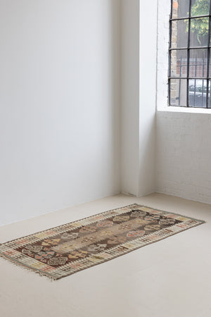 Close-up of an antique Anatolian kilim rug with geometric designs in brown, beige, and blue, featuring the traditional hand on hips motif