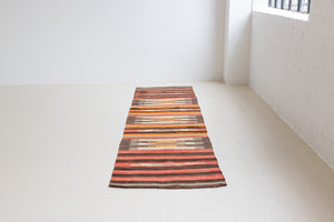 A South Anatolian nomadic kilim runner. Hand-woven on village and nomadic looms in vivid, naturally dyed colours, a tradition stretching back thousands of years. Vespa features a bold stripe pattern in earthy hues of rust, orange, taupe and black.