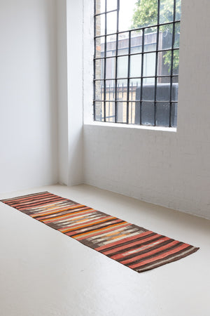 A South Anatolian nomadic kilim runner. Hand-woven on village and nomadic looms in vivid, naturally dyed colours, a tradition stretching back thousands of years. Vespa features a bold stripe pattern in earthy hues of rust, orange, taupe and black.