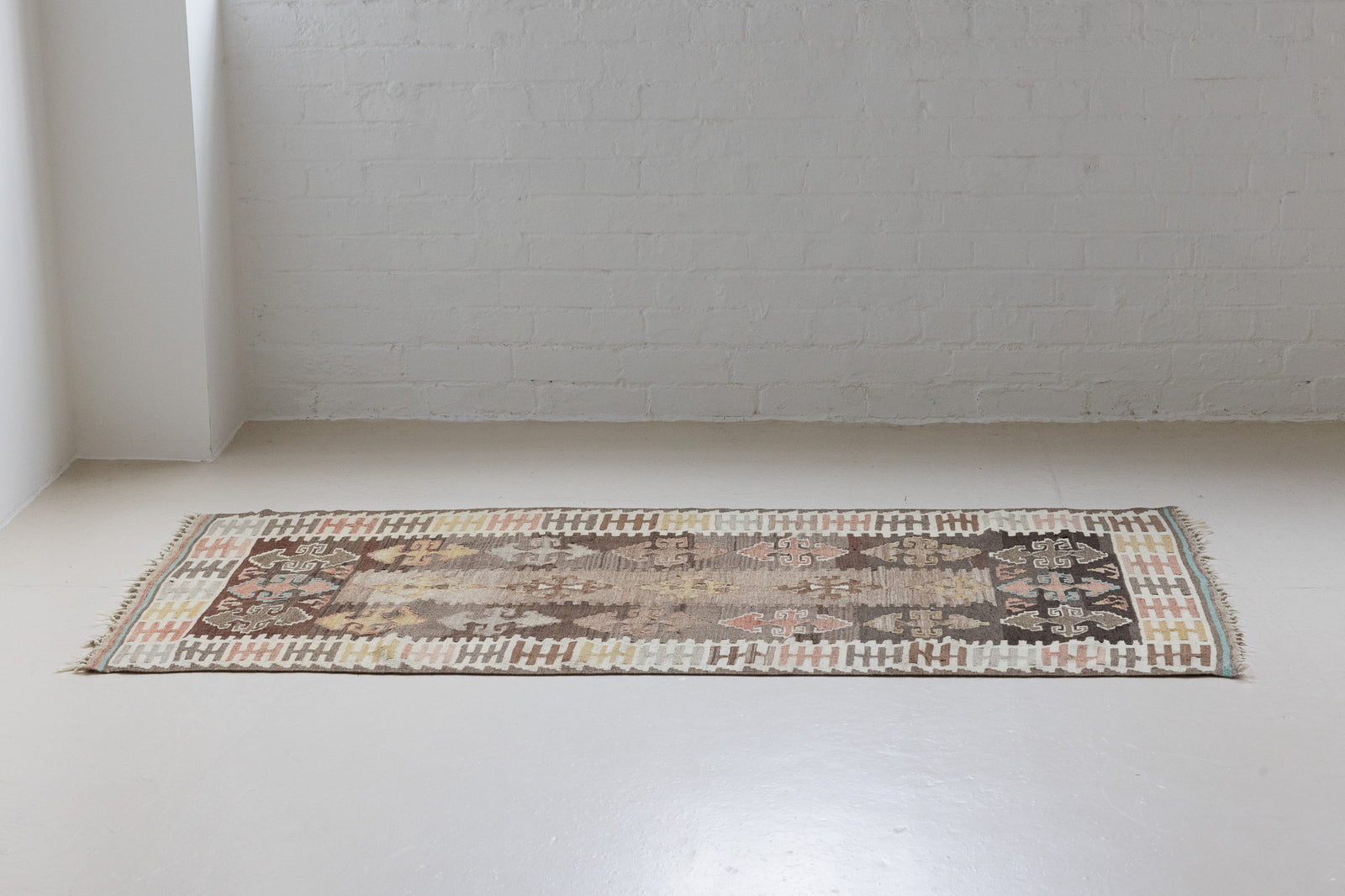 Nesa is a vintage Anatolian kilim rug with muted geometric designs on a white background