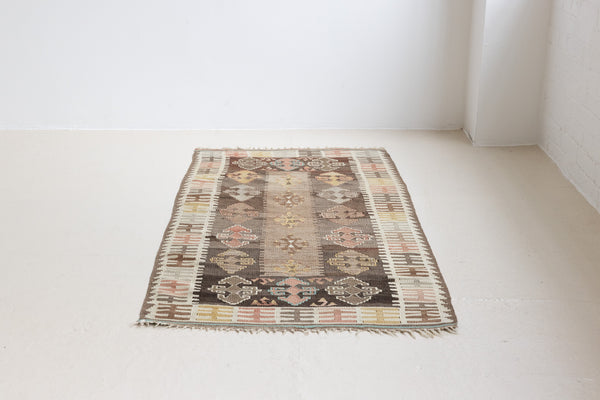 Close-up of a vintage Anatolian kilim rug with muted geometric designs on a white background