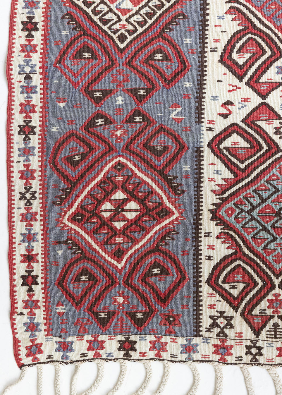 Zerrin is a bold, geometric Anatolian Hakkari kilim. Hand-woven on village and nomadic looms in vivid, naturally dyed colours, a tradition stretching back thousands of years. Kilims were woven for the practicalities of daily life and used as floor and wall coverings, storage bags, and prayer mats. Zerrin features a taupe and grey striped field scattered with the classic hand-on-hips motif, bordered by the comb motif both traditionally associated with marriage and fertility.