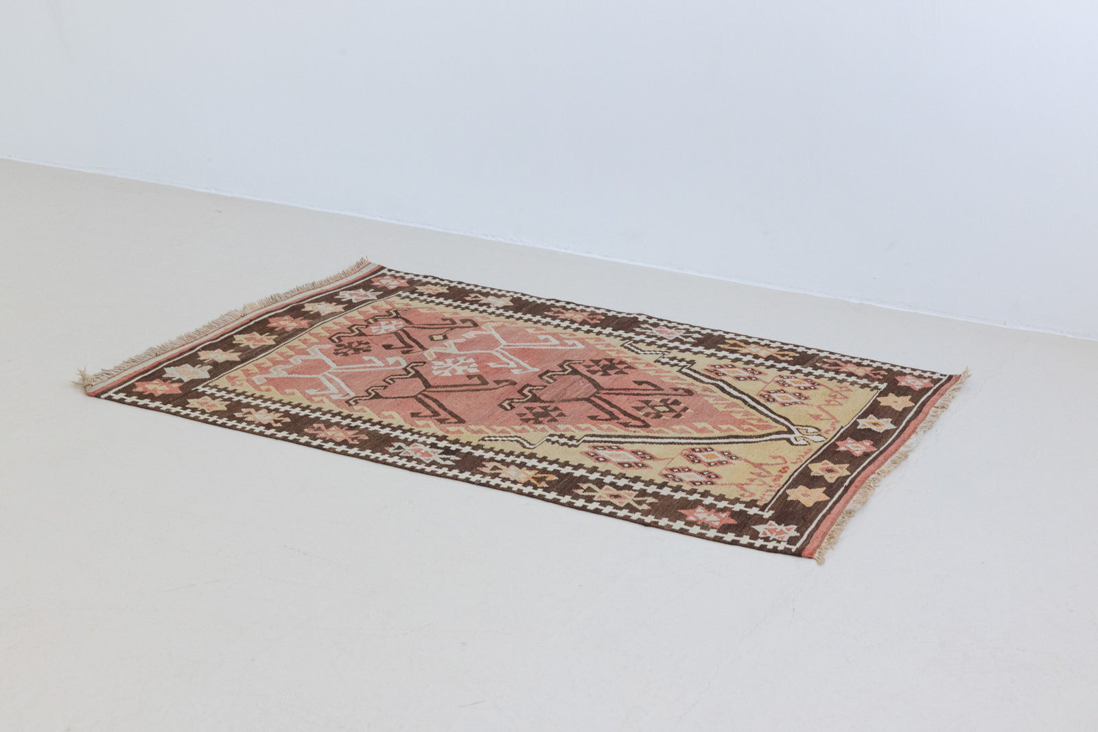 Delphi is a bold, geometric Anatolian kilim. Hand-woven on village and nomadic looms in vivid, naturally dyed colours, a tradition stretching back thousands of years. Kilims were woven for the practicalities of daily life and used as floor and wall coverings, storage bags, and prayer mats. Delphi features a rosey pink field scattered with a geometric motif. A black border is decorated with the Anatolian star motif traditionally associated with happiness.