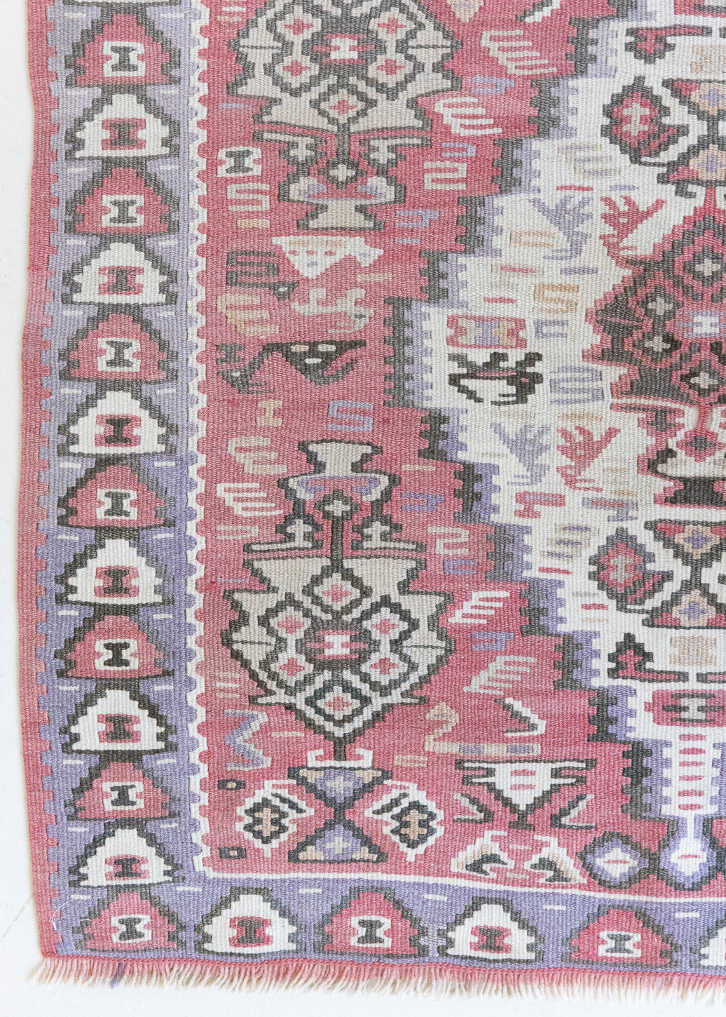 Melissa is an Anatolian Hakkari kilim rug with a Senneh design. Hand-woven on village and nomadic looms in vivid, naturally dyed colours. Kilims were woven for the practicalities of daily life and used as floor and wall coverings, storage bags, and prayer mats. Melissa features a soft pink field scattered with the classic Anatolian fertility motif, set within a soft purple border depicting the eye motif, traditionally used to protect from harm.