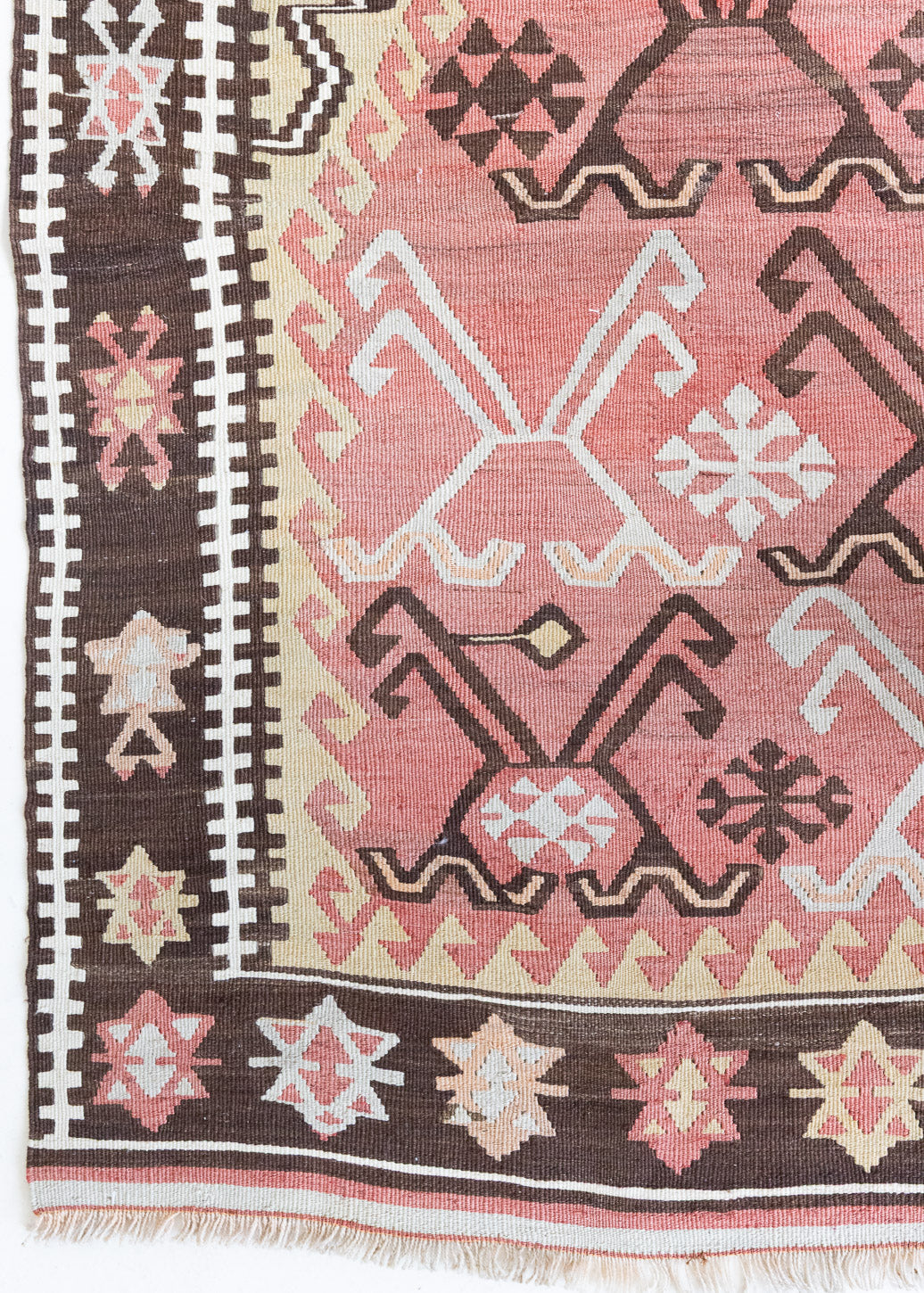 Delphi is a bold, geometric Anatolian kilim. Hand-woven on village and nomadic looms in vivid, naturally dyed colours, a tradition stretching back thousands of years. Kilims were woven for the practicalities of daily life and used as floor and wall coverings, storage bags, and prayer mats. Delphi features a rosey pink field scattered with a geometric motif. A black border is decorated with the Anatolian star motif traditionally associated with happiness.