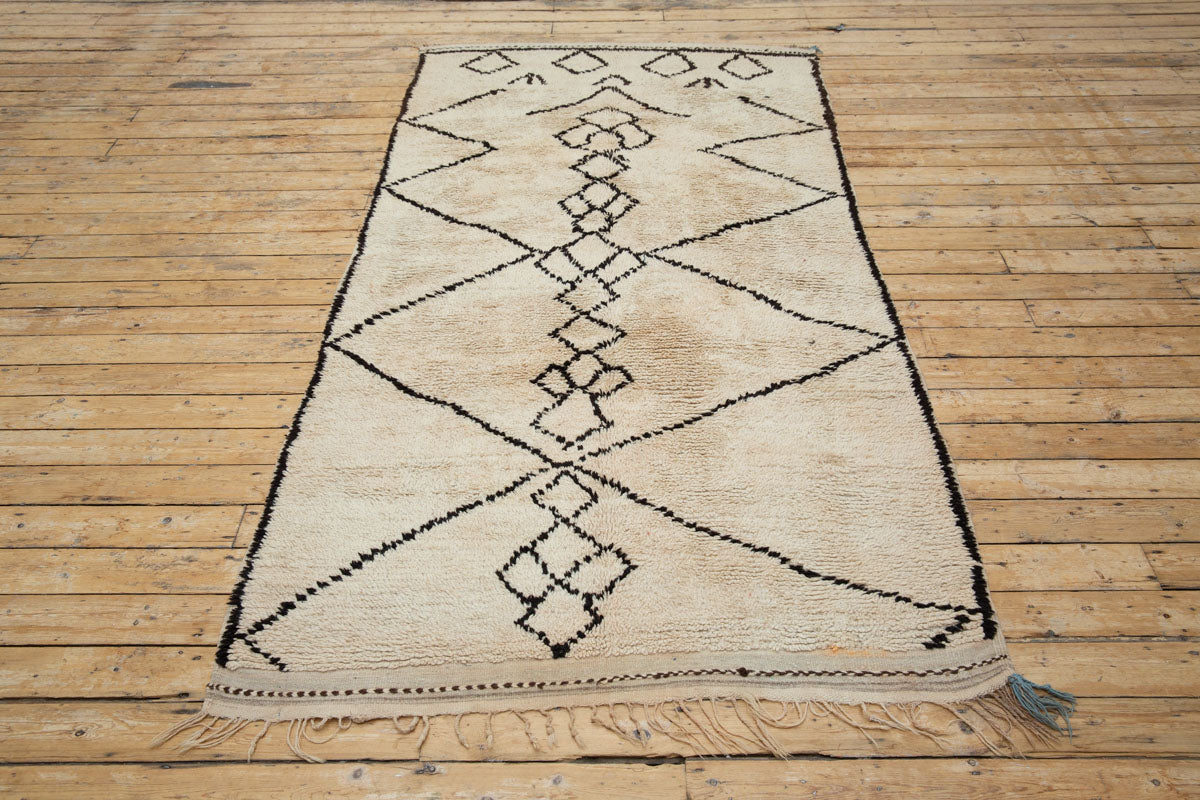 A traditional Azilal Moroccan rug featuring geometric patterns with black and beige colors on a beige background.