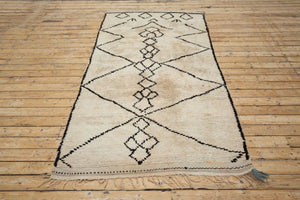 A traditional Azilal Moroccan rug featuring geometric patterns with black and beige colors on a beige background.