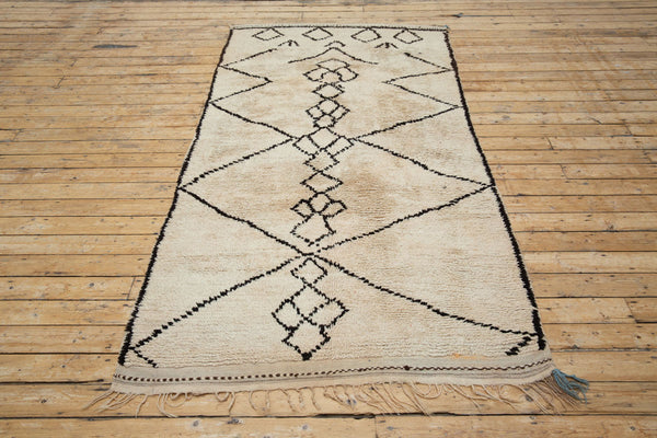 A traditional Azilal Moroccan rug featuring geometric patterns with black and beige colors on a beige background.