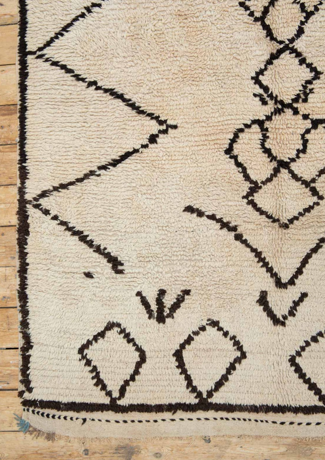 A traditional Azilal Moroccan rug featuring geometric patterns with black and beige colors on a beige background.