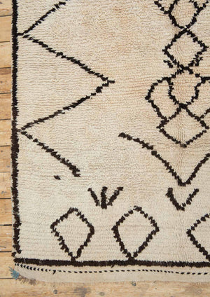 A traditional Azilal Moroccan rug featuring geometric patterns with black and beige colors on a beige background.